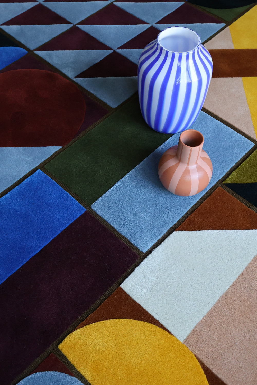 Two vases on a geometric-patterned rug with a colorful background
