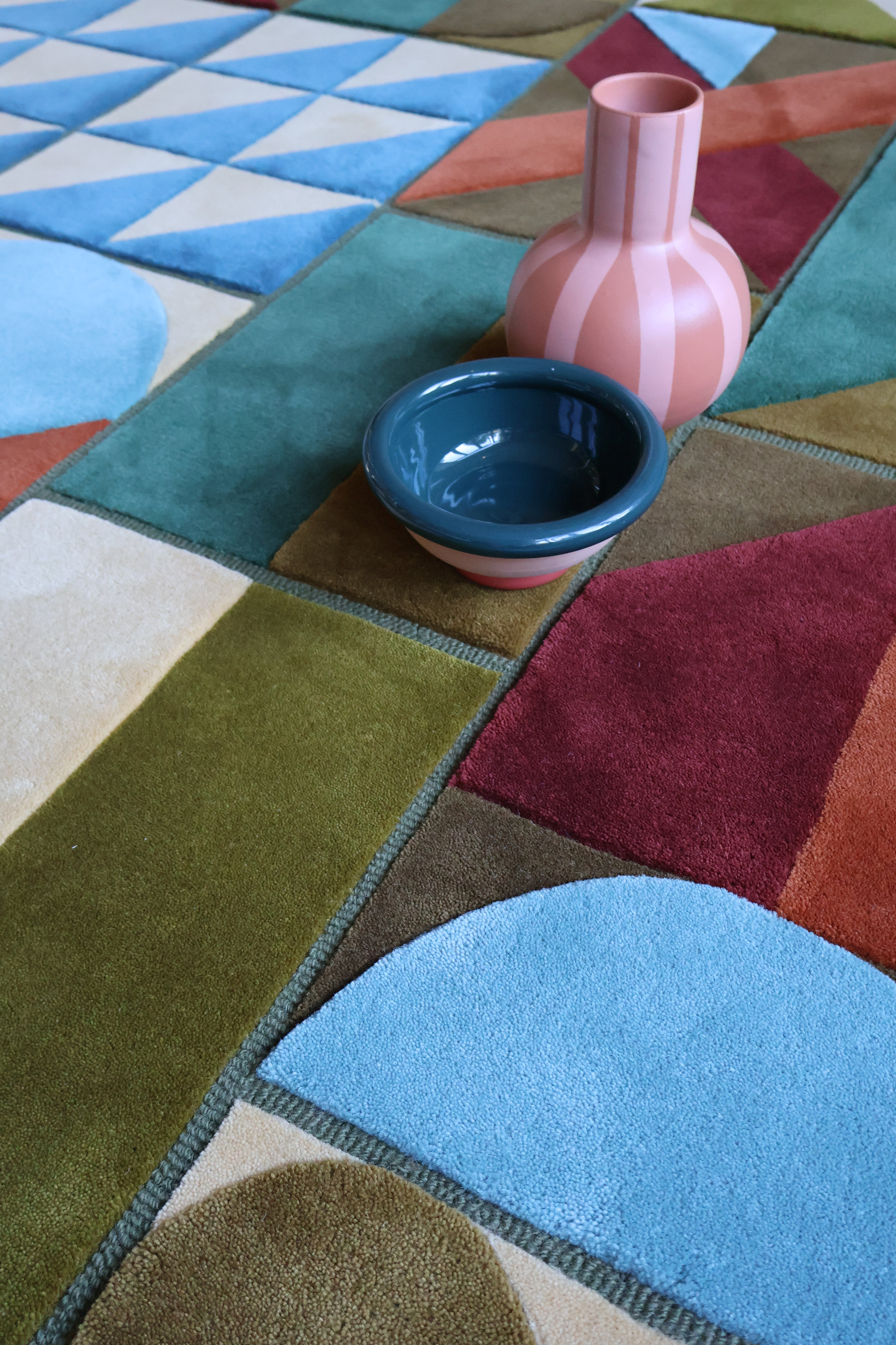 Colorful geometric-patterned rug with a pink vase and blue bowl on top