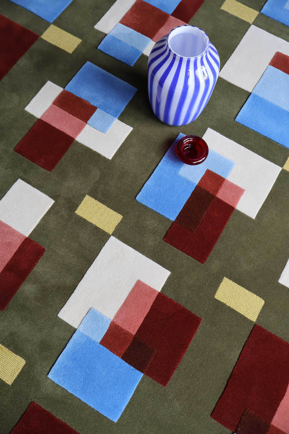 Colorful geometric-patterned rug with a striped vase and glass on top