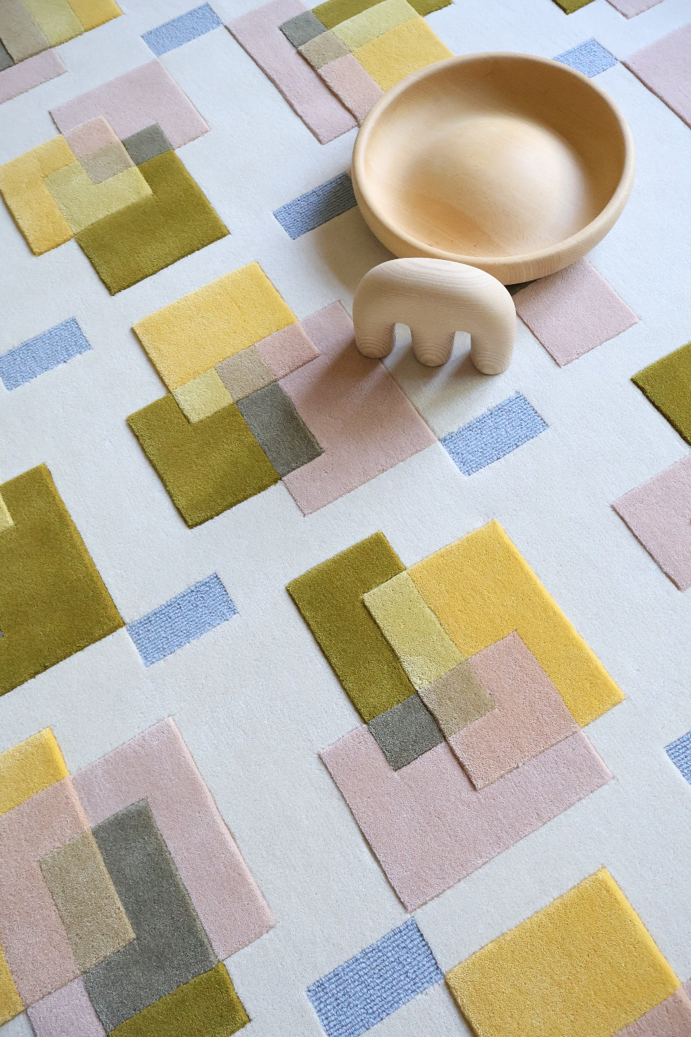 Colorful geometric-patterned fabric with a wooden bowl and elephant toy on top