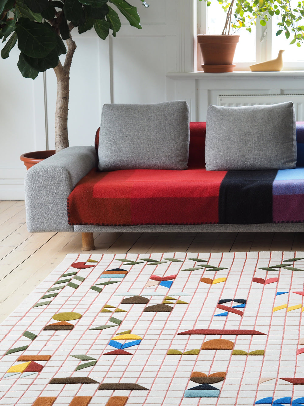 Colorful geometric-patterned rug in a living room with a sofa and plants.