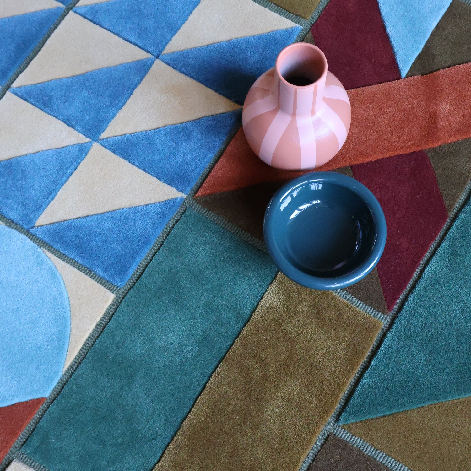 Echoes Colorful geometric-patterned rug with a pink vase and blue cup on top